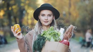 年轻漂亮的女人穿着时髦的外套站在公园里，手里拿着<strong>一包</strong>产品，微笑着看着。